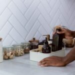 A person tidily organizes a kitchen counter with reusable glass jars and bottles.