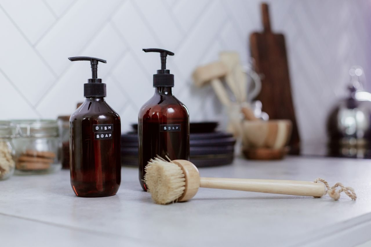 Aesthetic kitchen setting featuring amber soap bottles and dish brush for elegant cleaning.