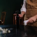 A waitress in an apron cleaning a table with a spray bottle and cloth in a dimly lit restaurant.