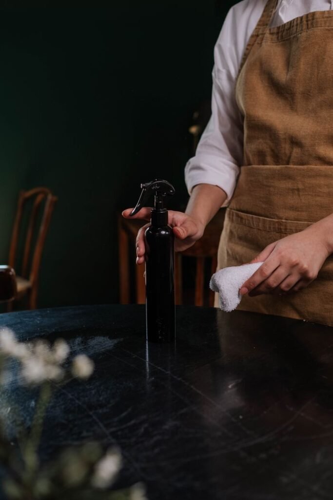 A waitress in an apron cleaning a table with a spray bottle and cloth in a dimly lit restaurant.